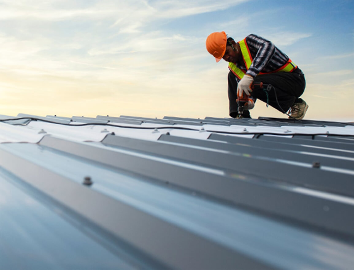 A roofer fastening panels on a metal roof